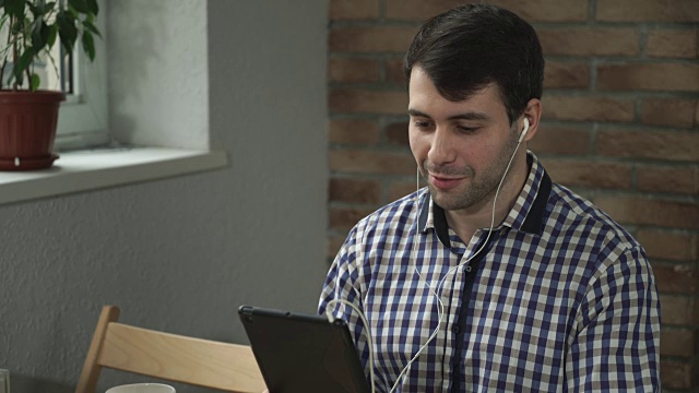 一名手持平板电脑的男子戴着耳机，欢迎同伴在线视频下载