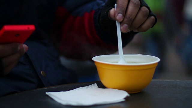 在寒冷多风的天气里，穷人在户外喝热汤，视频素材