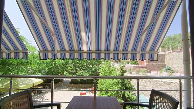夏季酒店的遮阳阳台，室外桌椅设置在可伸缩遮阳棚的凉阴处视频素材