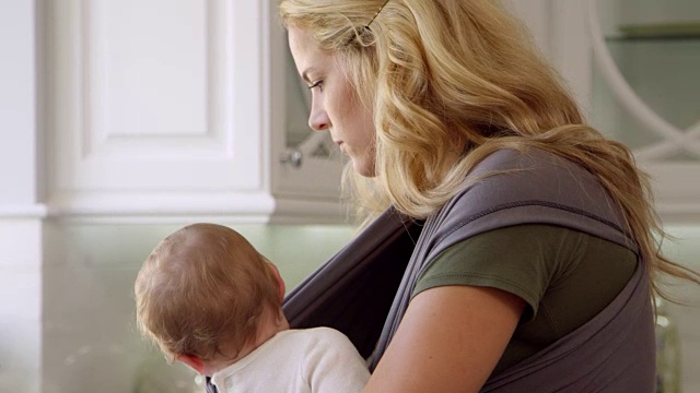 忙碌的母亲与婴儿在吊带在家拍摄的R3D视频素材