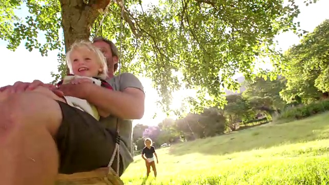 父亲和他笑着的儿子在秋千上享受夏天的日落视频素材