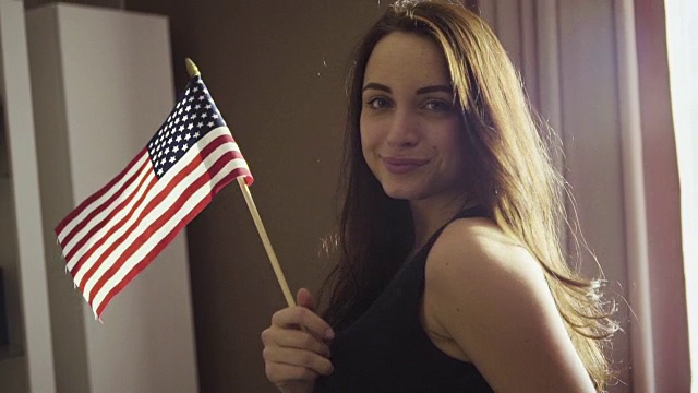 慢镜头镜头里年轻的白人女性站在房间里挥舞着美国国旗。视频下载