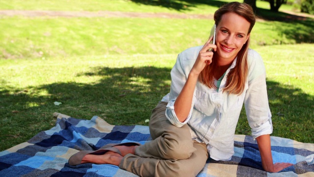 一个金发美女坐在公园里的毯子上聊天视频素材