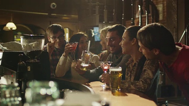 朋友们开怀大笑，喝着啤酒和鸡尾酒，一起在酒吧度过美好时光。视频素材