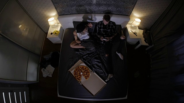年轻的一对爱吃披萨和玩电子游戏。俯视图视频下载