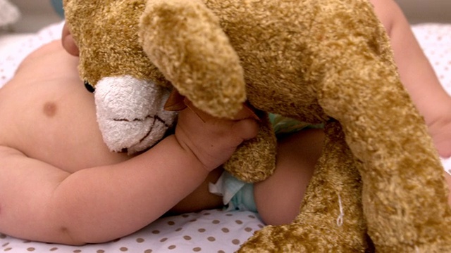 婴儿躺在婴儿床上，用奶嘴吮吸着泰迪熊视频素材