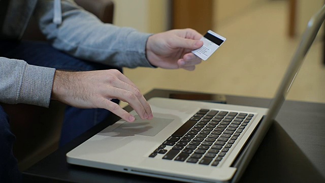 男人付账单，网上购物，插入信用卡号码。一名男子使用笔记本电脑和信用卡在网上购物。近距离视频素材