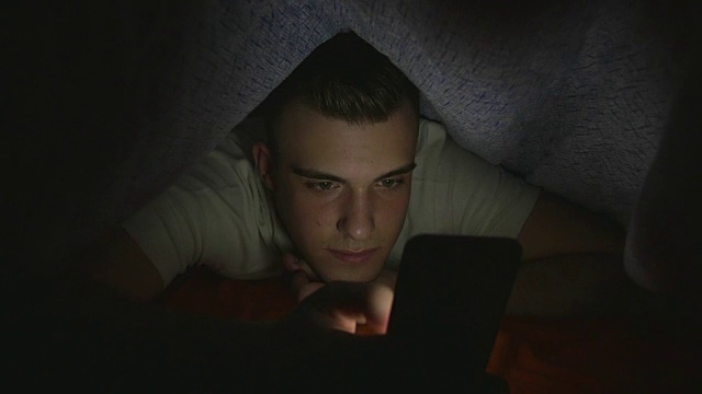 有魅力的年轻人在床上玩智能手机视频下载