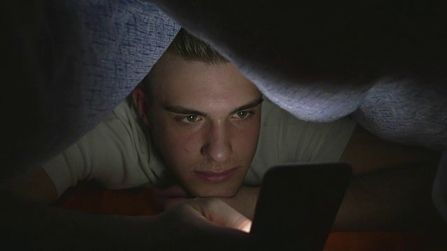 有魅力的年轻人在床上用智能手机浏览社交媒体视频下载