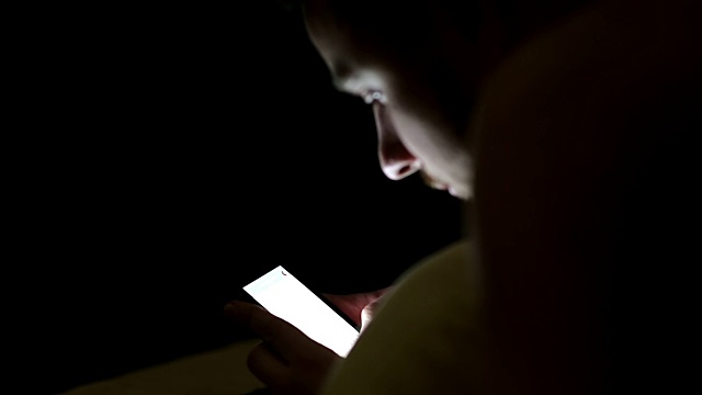 年轻人晚上在床上盖着毯子使用智能手机视频下载