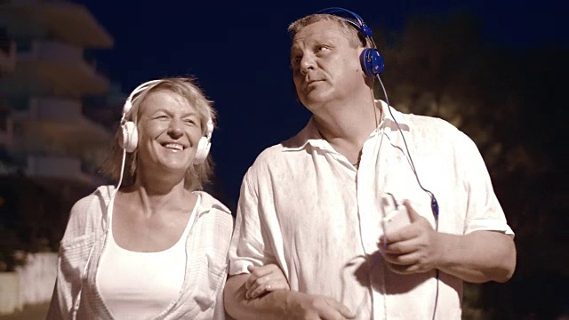 老年夫妇在夜间散步时听音乐视频素材
