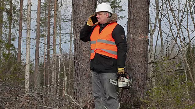 伐木工人用链锯在树旁用智能手机聊天视频下载