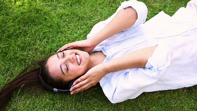 漂亮的女孩躺在草地上听音乐视频素材