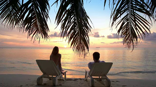一对夫妇在热带海滩上欣赏日落。视频素材