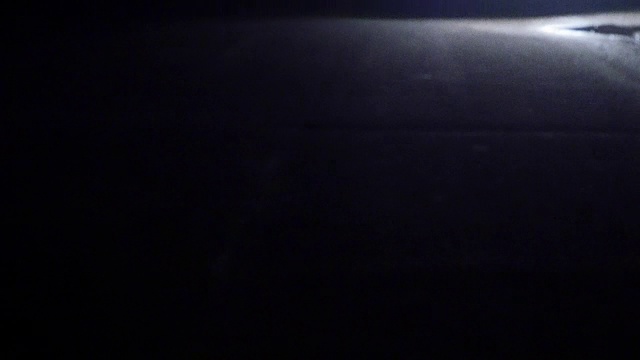 汽车在晚上离开转弯处。在一片漆黑中，只能看到汽车前灯的亮光。视频素材