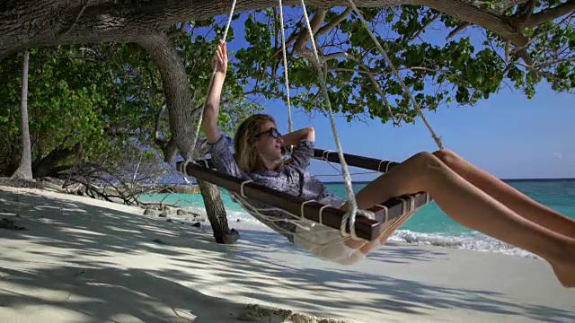 一名年轻女子在热带海滩的吊床上享受着海浪的声音。视频素材