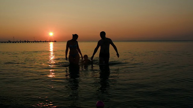 夕阳西下，一家人的剪影出现在海面上三个人视频素材
