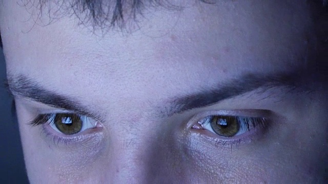 近距离的男人脸阅读互联网，与屏幕在她的眼睛在晚上的反射视频素材