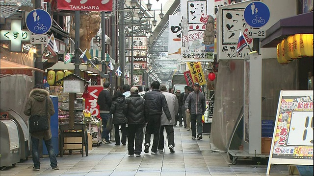 日本大阪，行人穿过新世街市中心Tsutenkaku大厦附近。视频素材