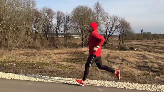 一个穿着红色衣服的运动员在公园的小路上奔跑，摄像机一直跟着他视频下载