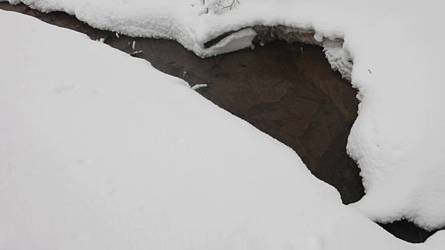 冬天森林里的小溪穿过蓬松的雪堆。下雪了。树上覆盖着雪帽。视频素材