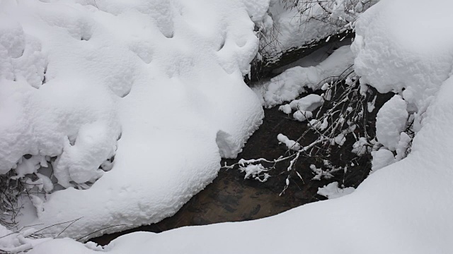 冬天森林里的小溪穿过蓬松的雪堆。下雪了。树上覆盖着雪帽。视频素材