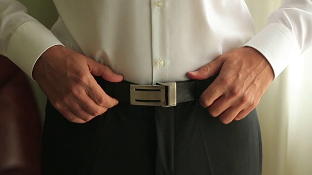 一个新郎调整他裤子上的腰带的特写。婚礼的准备工作。视频下载