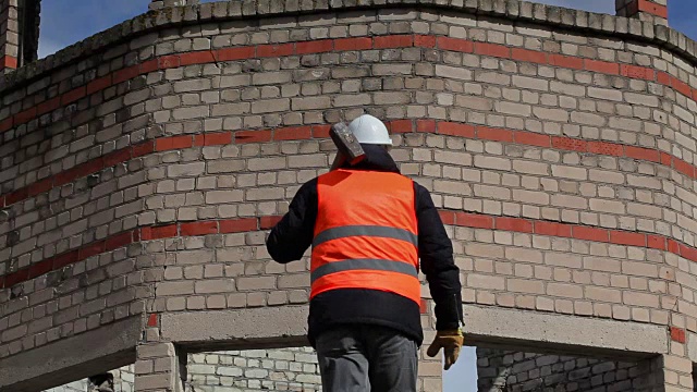 一名工人用大锤呼叫砖墙附近的其他工人视频素材