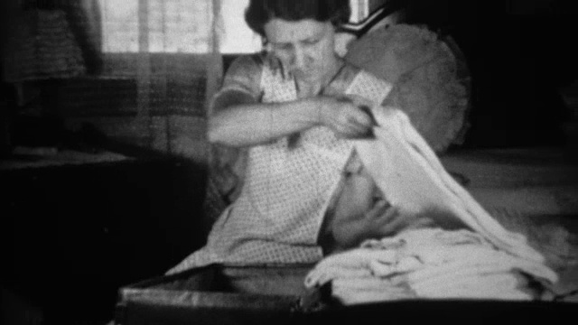 1936年:一名女子坐在客厅里把衣服装进行李箱。视频素材