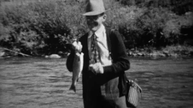 1939年:渔夫涉过湍急的溪流，展示钓到的鳟鱼。视频素材