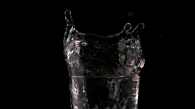 在黑色背景下，冰块落入一杯水中视频素材