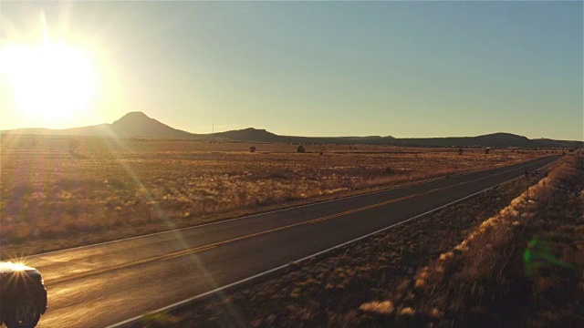 图片:金色的夏日夕阳下，一辆黑色SUV行驶在空旷的乡村道路上视频素材