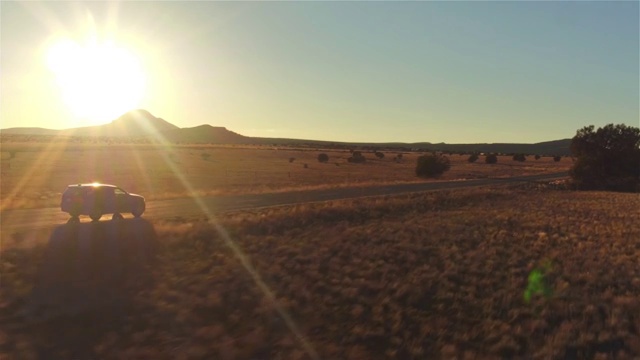 图片:金色的夏日夕阳下，一辆黑色SUV行驶在空旷的乡村道路上视频素材