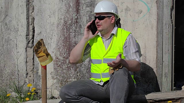愤怒的建筑工人在墙边用智能手机打电话视频下载
