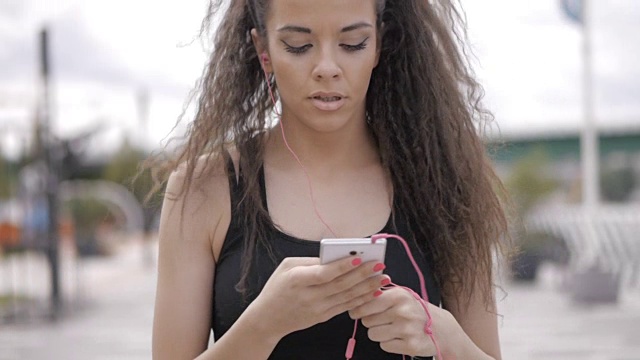 美丽的黑发，卷曲的健身模特，设置在她的智能手机上的秒表和跑在焦点。浅景深，聚焦前景视频素材