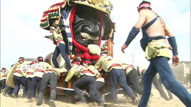 在一场游行中，参与者们推着一辆在沙子中漂浮的Karatsukunchi Hikiyama。视频素材