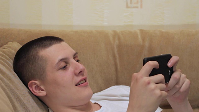 一个男人躺在沙发上，手里拿着一个智能手机视频素材