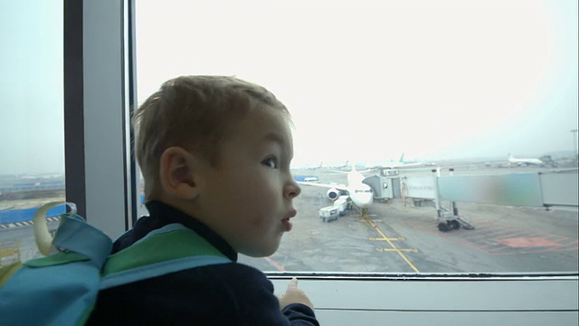 小男孩望着窗外，指着飞机视频素材
