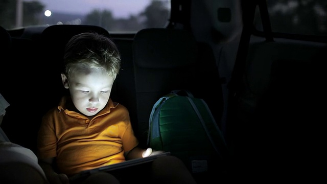 小男孩晚上开车时用平板电脑视频下载
