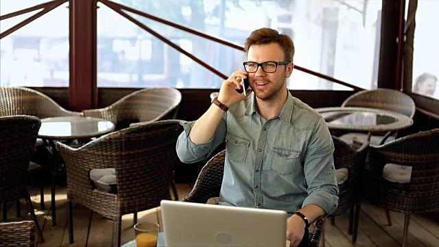 一个自信的年轻人坐在咖啡馆里一边打电话一边微笑视频素材