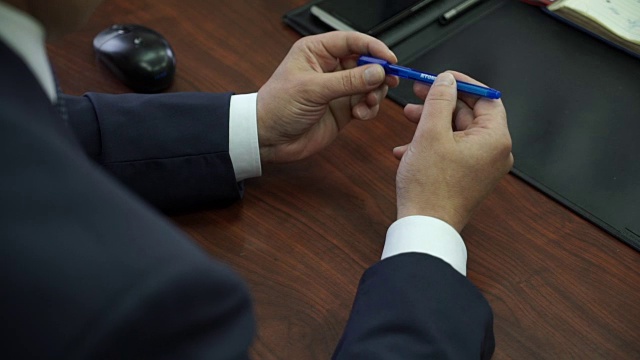 一个男人坐在会议室里，紧张地转动着手里的笔视频下载