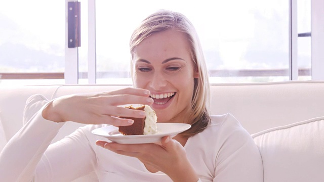 金发女人微笑着坐在沙发上吃蛋糕视频下载