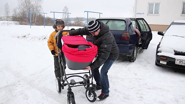 父亲组装红色婴儿车，儿子帮助他。视频下载