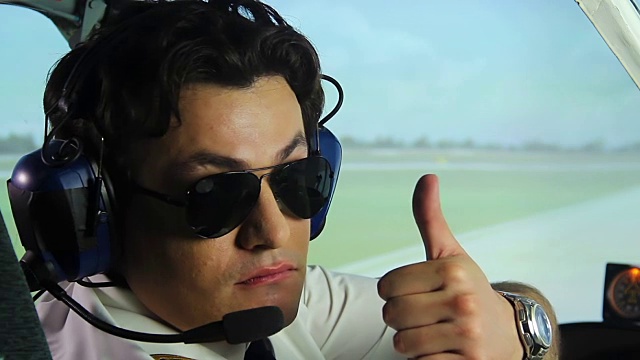 专业飞行员戴墨镜，头戴耳机坐在驾驶舱前飞行视频素材