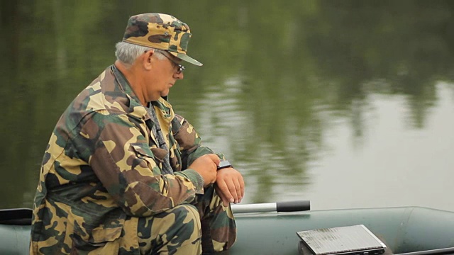 男人在湖上触摸智能手表。一个拿着钓竿在充气船上的渔夫视频下载