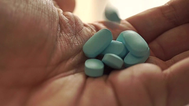 一名男子将一堆蓝色药丸从他的手掌上的罐子里倒入微距慢镜头视频下载