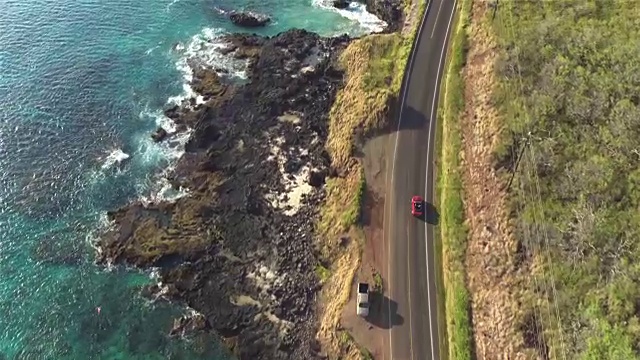 航拍:红色敞篷车在岩石海洋悬崖上令人惊叹的海岸公路上行驶视频素材