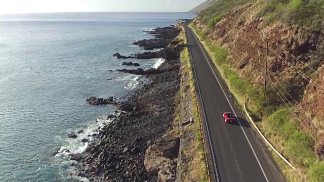 一辆红色敞篷车在岩石海岸上的海岸公路上行驶视频素材