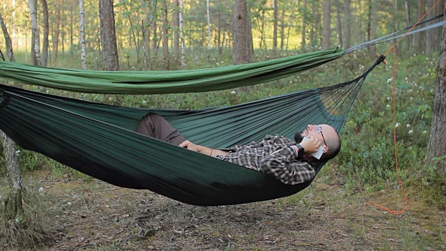 一个躺在吊床上的男人正在打电话。树林里那个留着胡子戴眼镜的男人视频下载