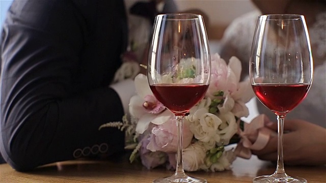 两杯红酒在一对美丽的新婚夫妇的背景上。慢动作视频下载